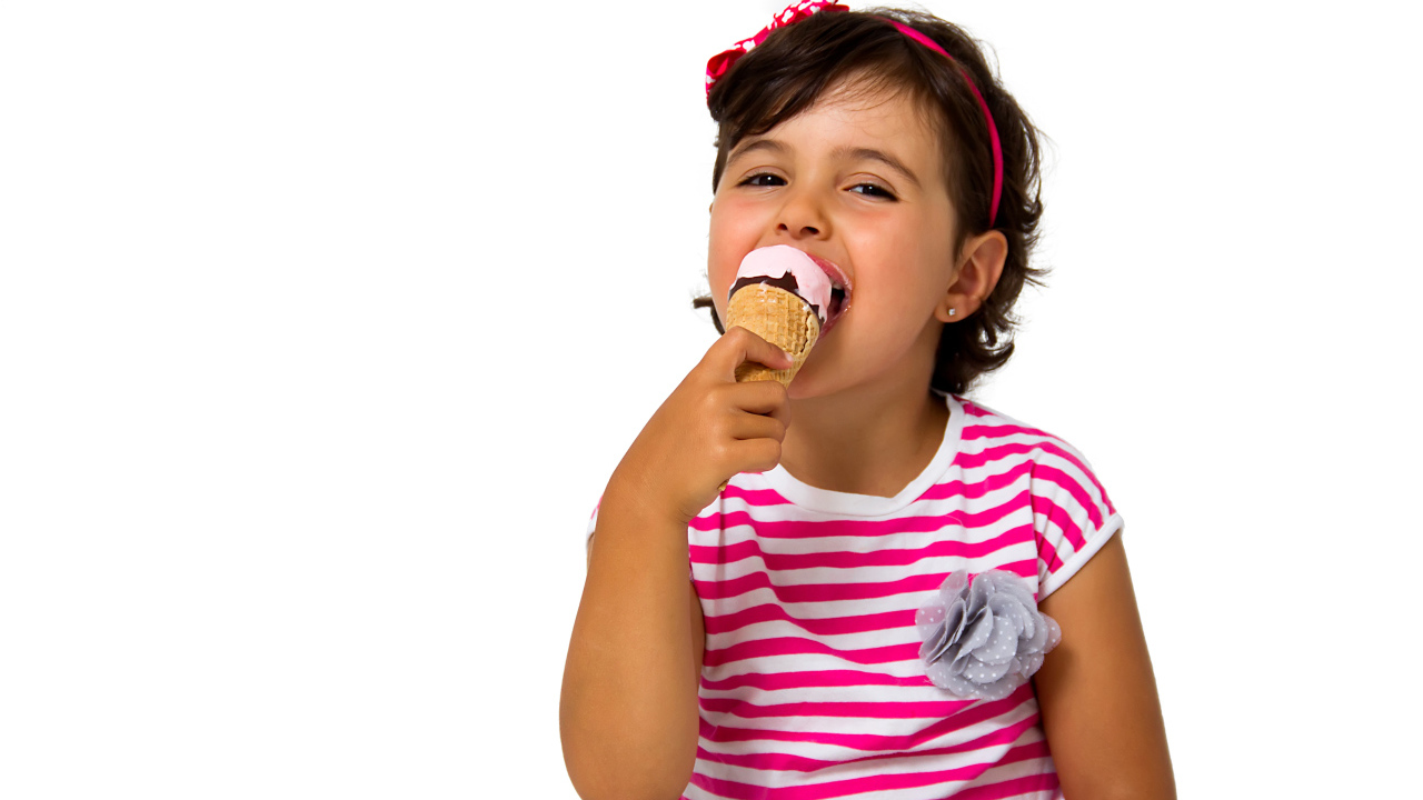 Маленькая девочка ест мороженое за столом на белом фоне