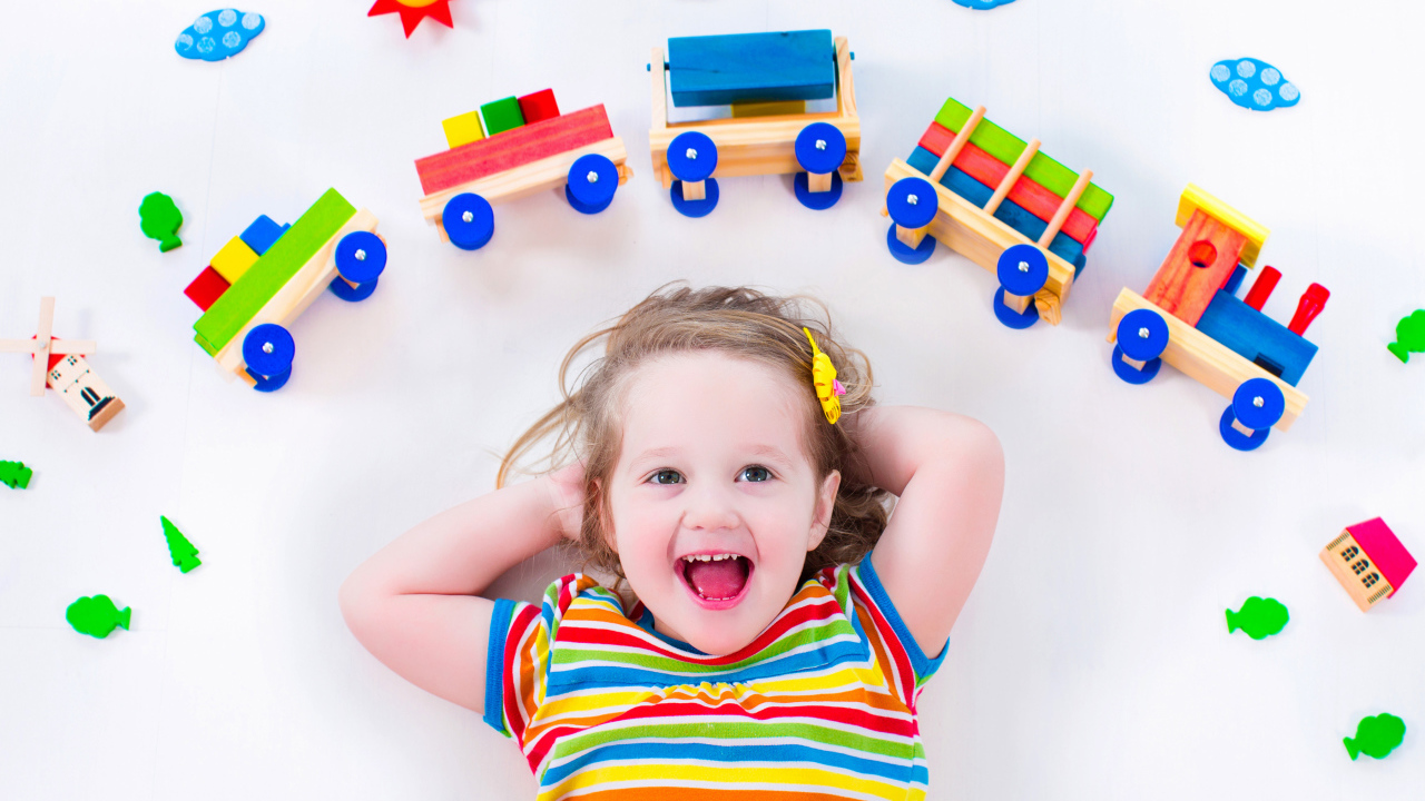 Маленькая девочка на сером фоне с игрушечным паровозом 