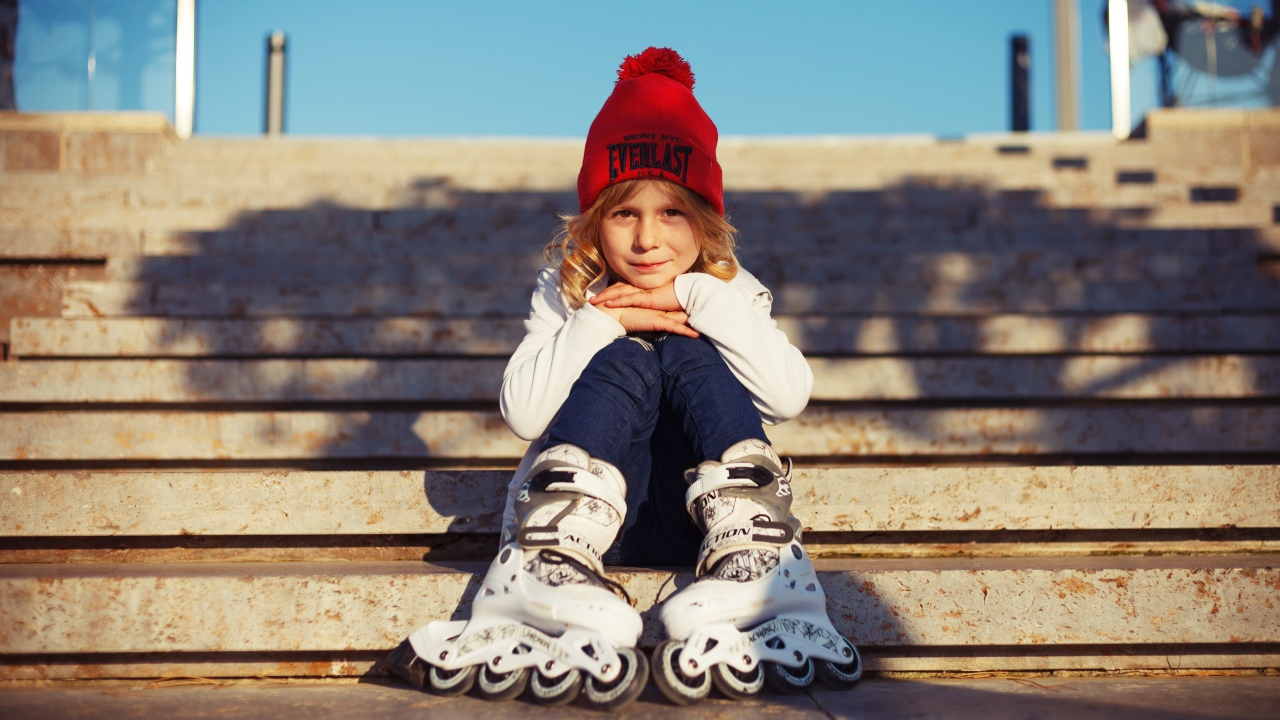 Маленькая девочка в роликах сидит на ступеньках 