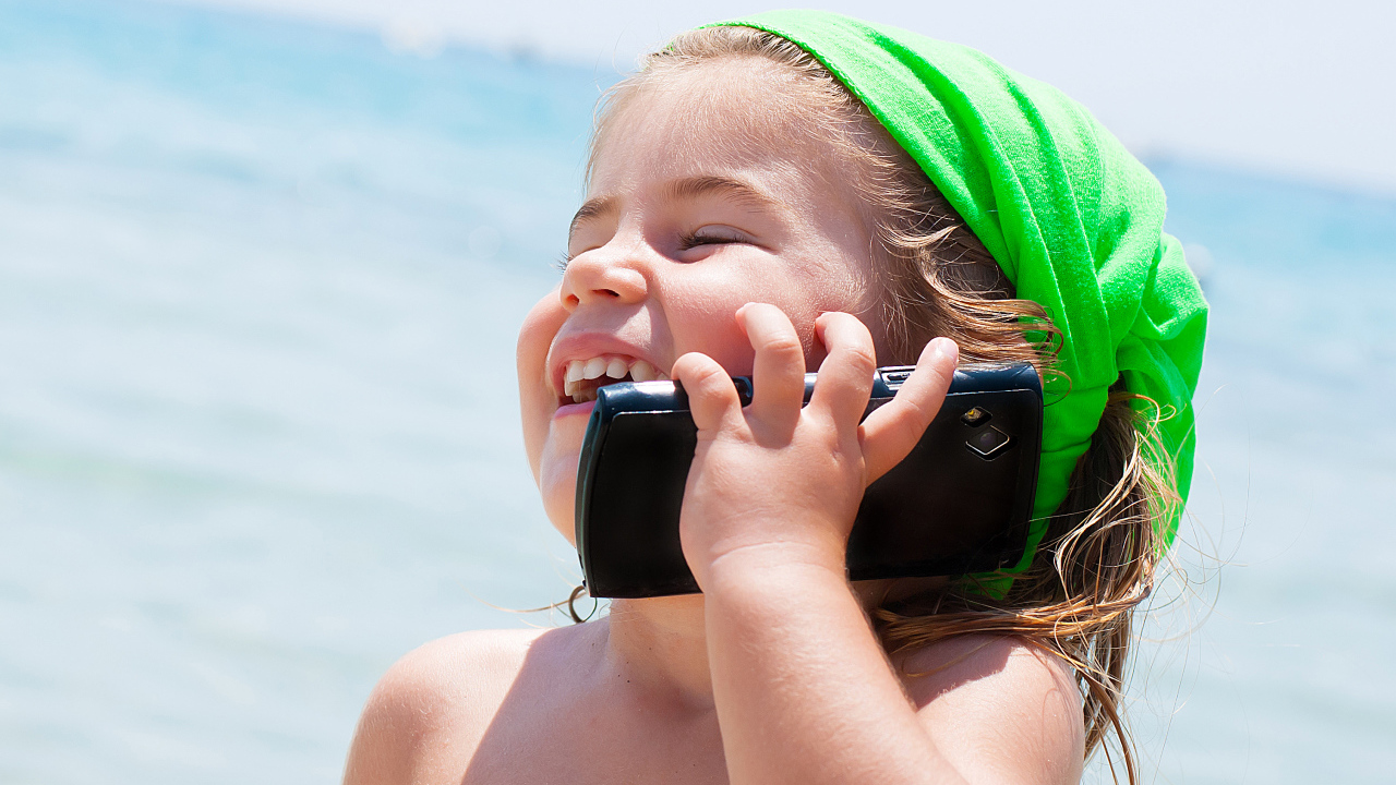 Маленькая девочка с телефоном на пляже