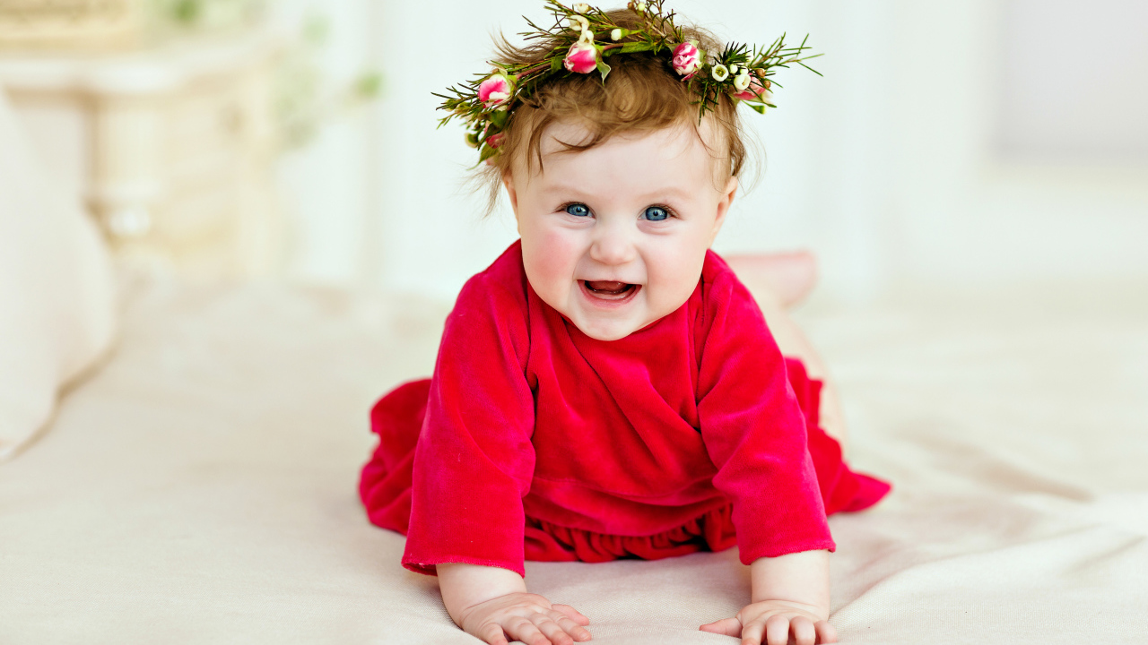 Маленькая улыбающаяся девочка в красном платье с венком на голове