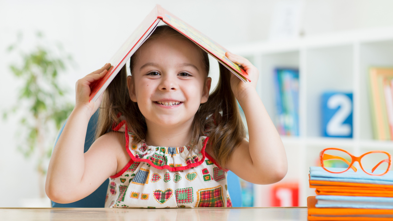 Маленькая улыбающаяся девочка с книгой на голове