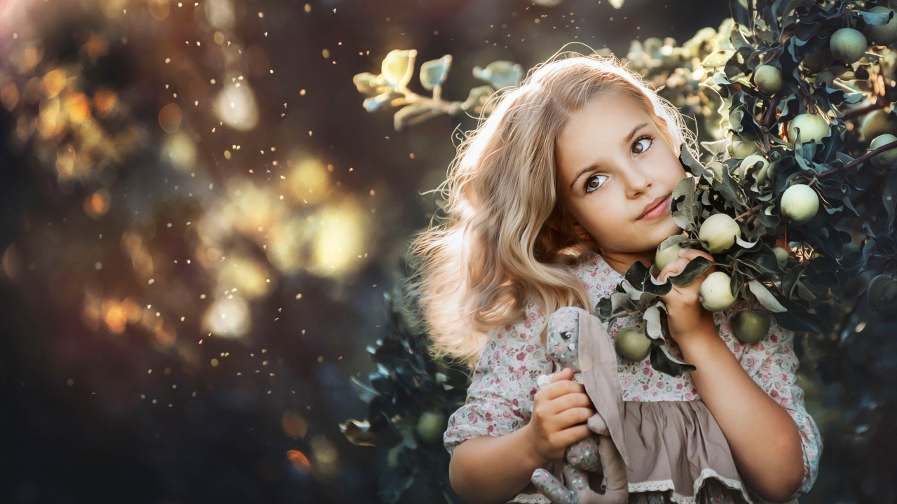 Маленькая девочка стоит у ветки с яблоками