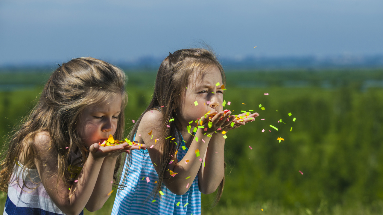 Две маленькие девочки сдувают конфетти  с рук