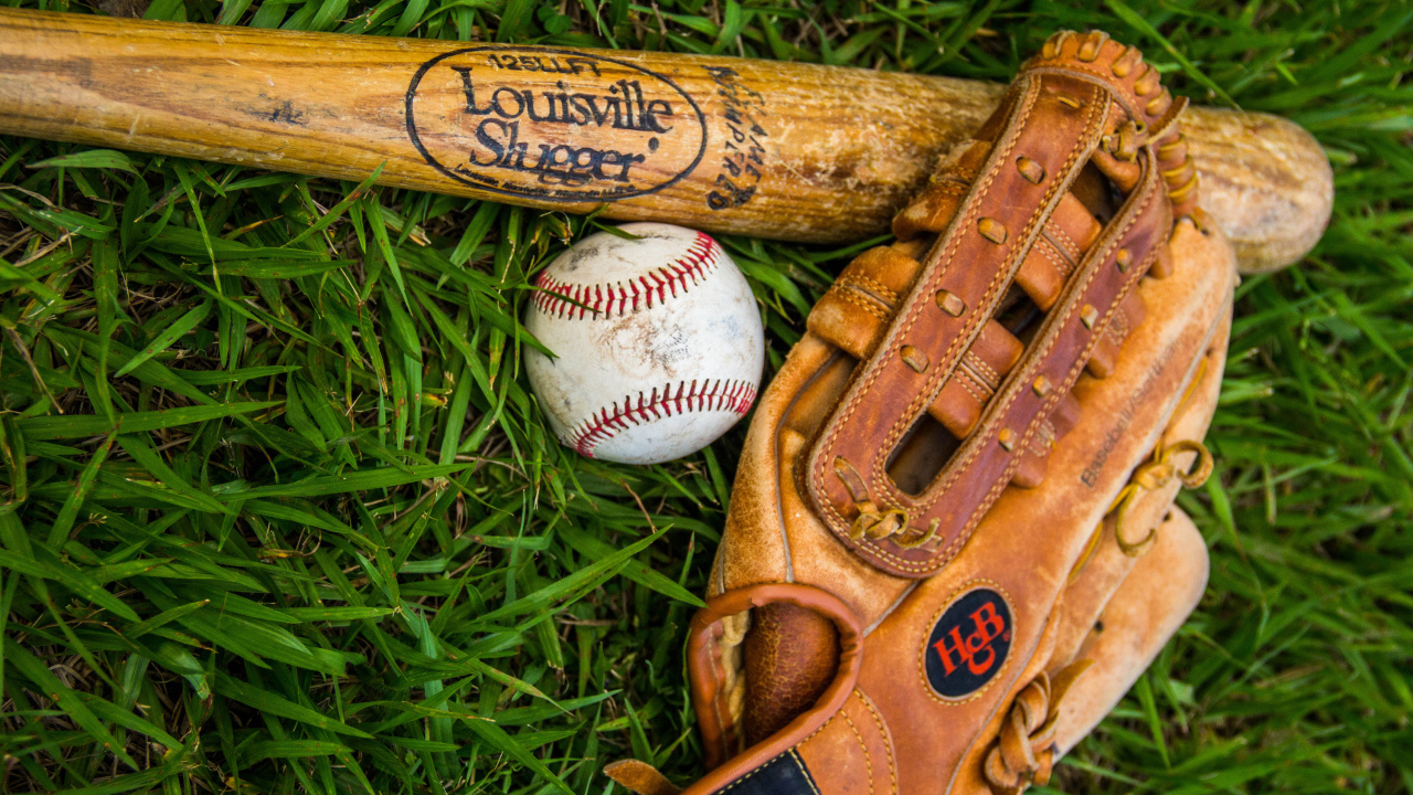 Бейсбольная бита, перчатка и мяч лежат на зеленой траве