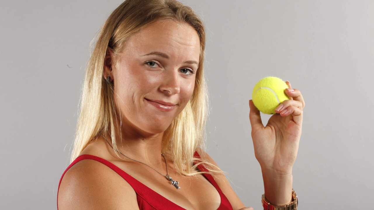 Датская теннисистка Каролина Возняцки с мячиком в руке на сером фоне