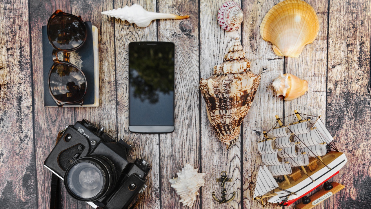 Фотоаппарат, смартфон, ракушки, очки и паспорт на столе