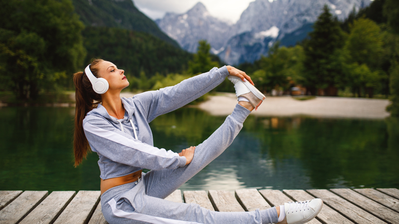 Girl in headphones doing gymnastics on a bridge by the lake