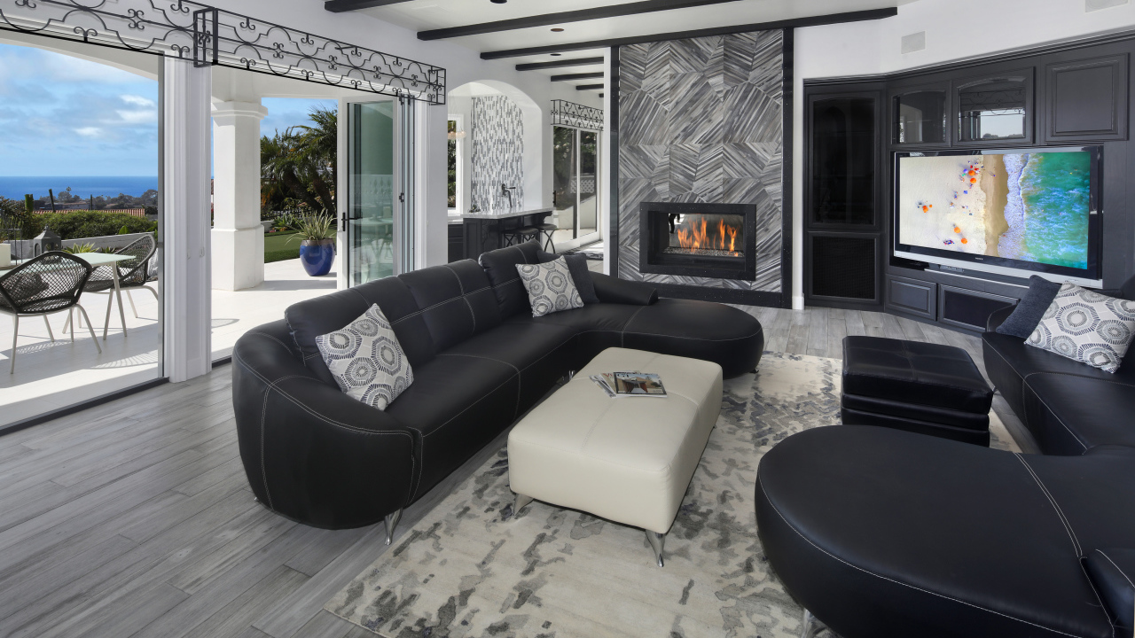 Большая просторная гостиная с черными кожаными диванами, телевизором и камином 
