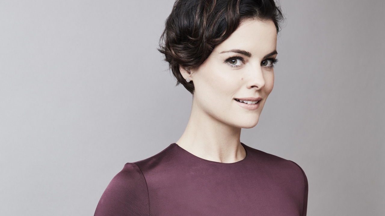 Улыбающаяся девушка, актриса Джейми Александр на сером фоне