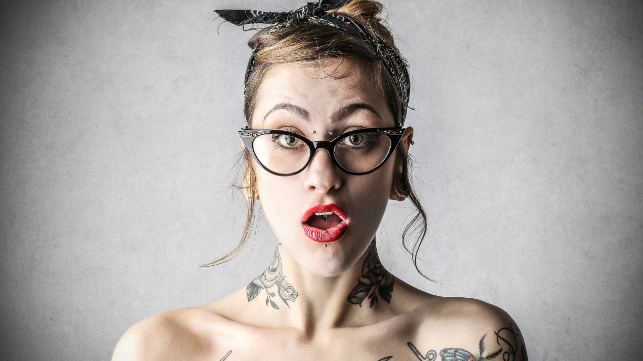 Удивленная девушка в очках с татуировками на теле
