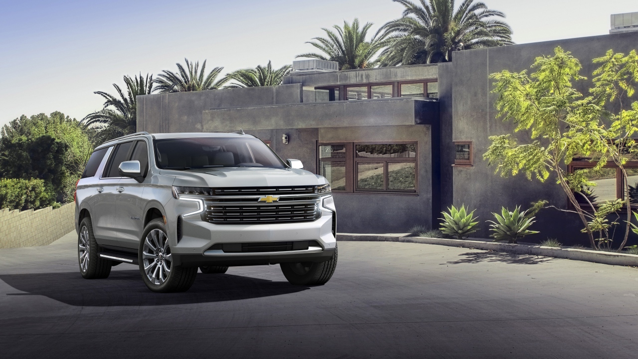 Серый внедорожник Chevrolet Suburban, 2021 года на фоне дома