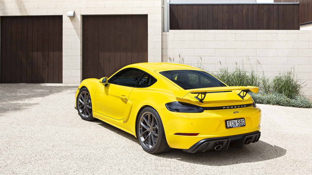 Желтый автомобиль Porsche 718 Cayman GT4, 2020 года у гаража 
