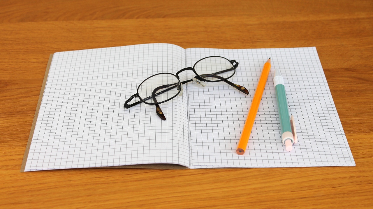Notebook, pen, pencil and glasses are on the desk