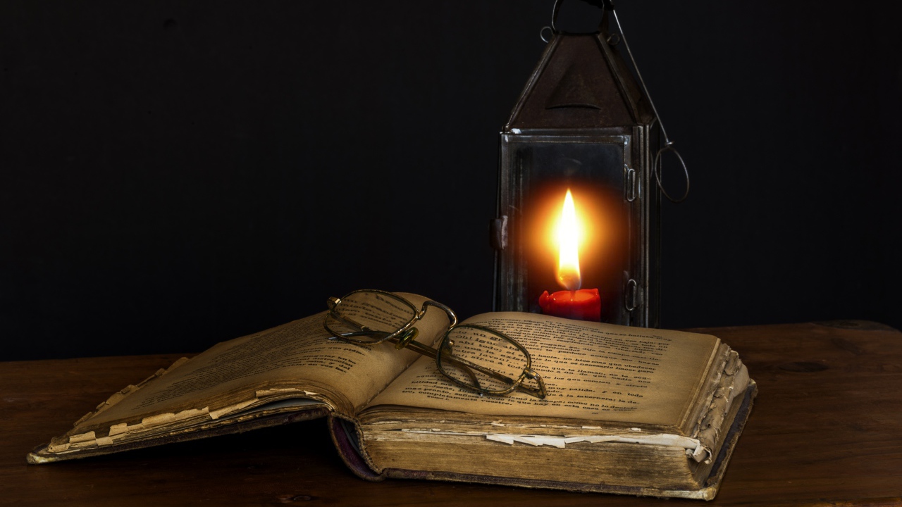 Old book on table with glasses and lamp
