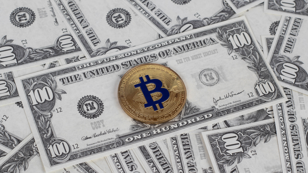 Монета Биткоин лежит на стодолларовых купюрах