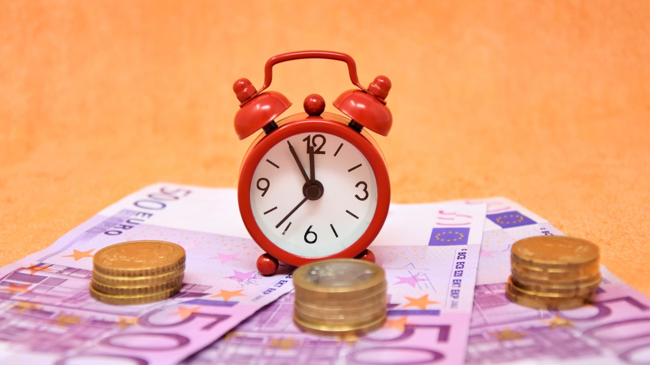 Маленький красный будильник с купюрами евро и монетами