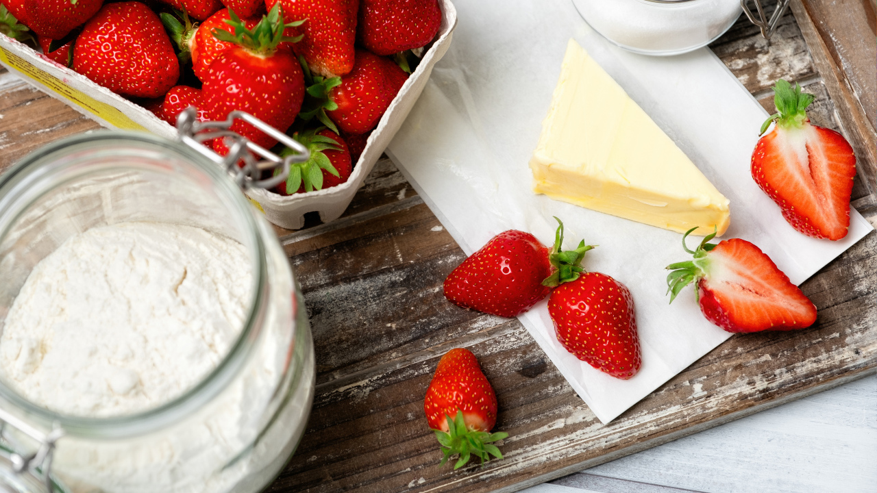 Кусок масла на столе с клубникой и мукой 