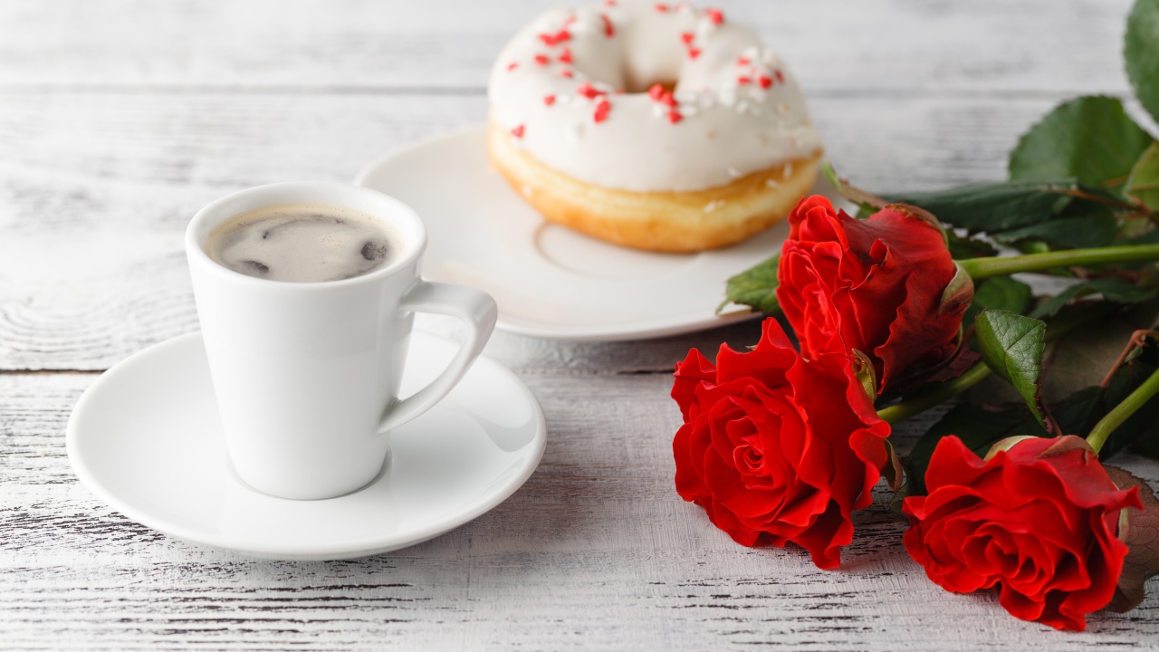 Cup of coffee, a donut and three red roses on the table