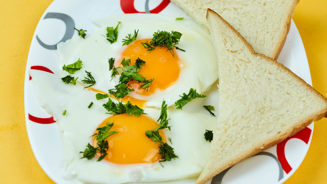 Яичница глазунья с зеленью на тарелке с хлебом 