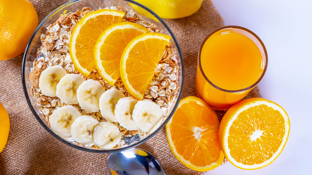 Овсяные хлопья в тарелке с кусочками банана и апельсина на столе с соком