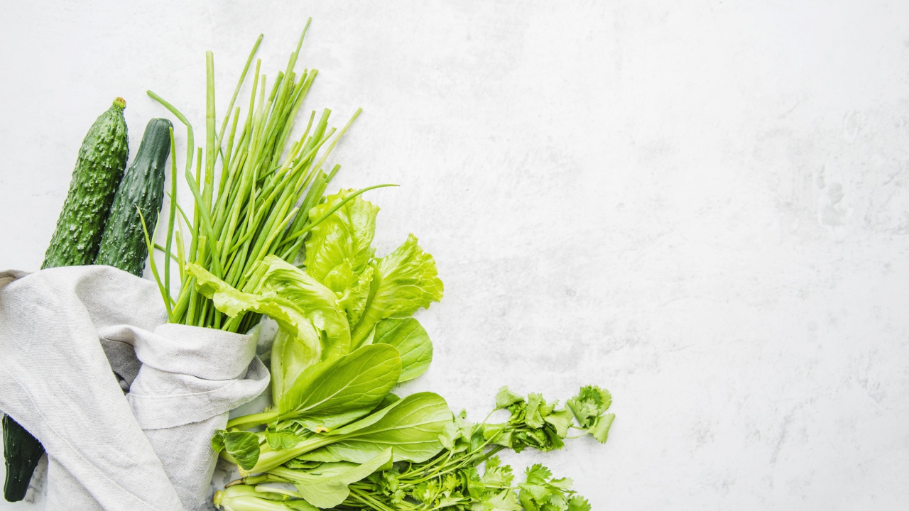 Зелень петрушки и лука, листья салата и свежие огурцы на белом фоне