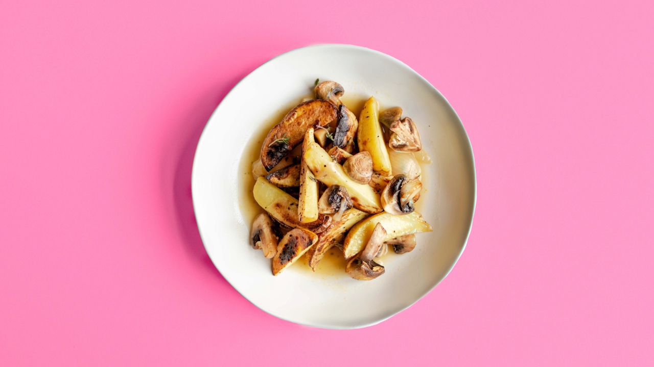 Картофель с грибами в тарелке на розовом фоне 