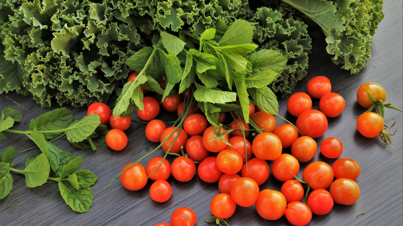 Красные мелкие помидоры на столе с зеленью 