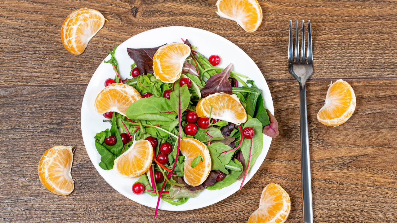 Салат из зелени и мандарина на белой тарелке на столе с вилкой