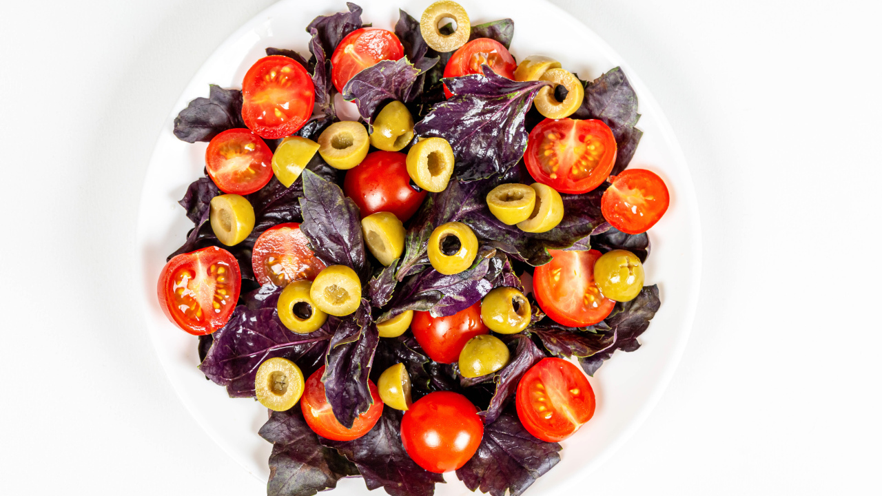 Салат с листьями базилика, помидорами и оливками на белом фоне