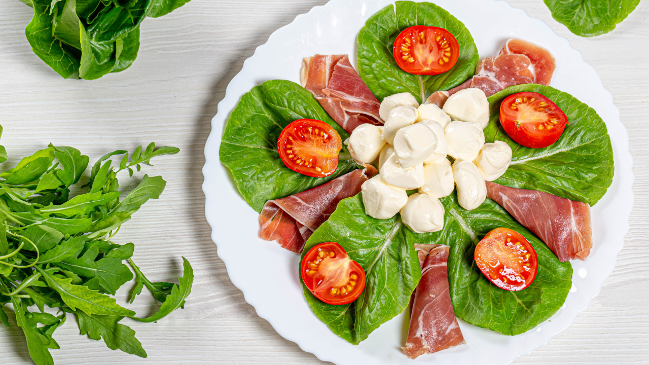 Кусочки ветчины на тарелке с сыром, помидорами и листьями салата