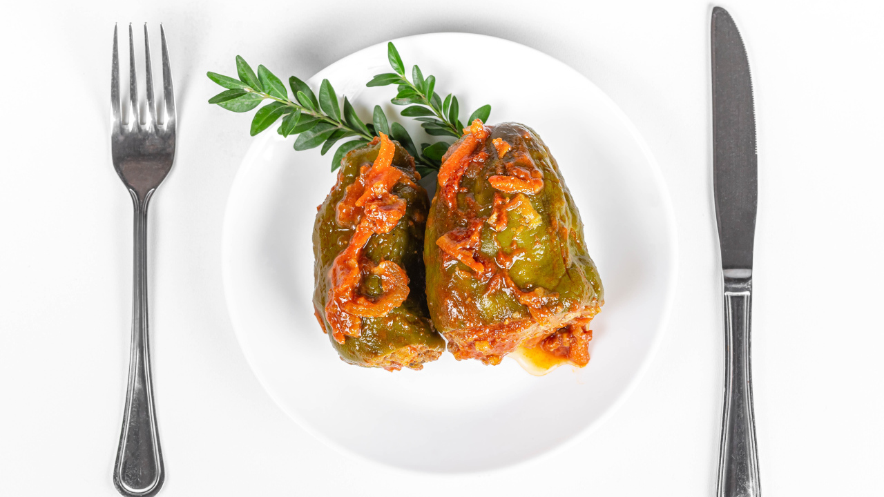 Фаршированный перец на белой тарелке со столовыми приборами