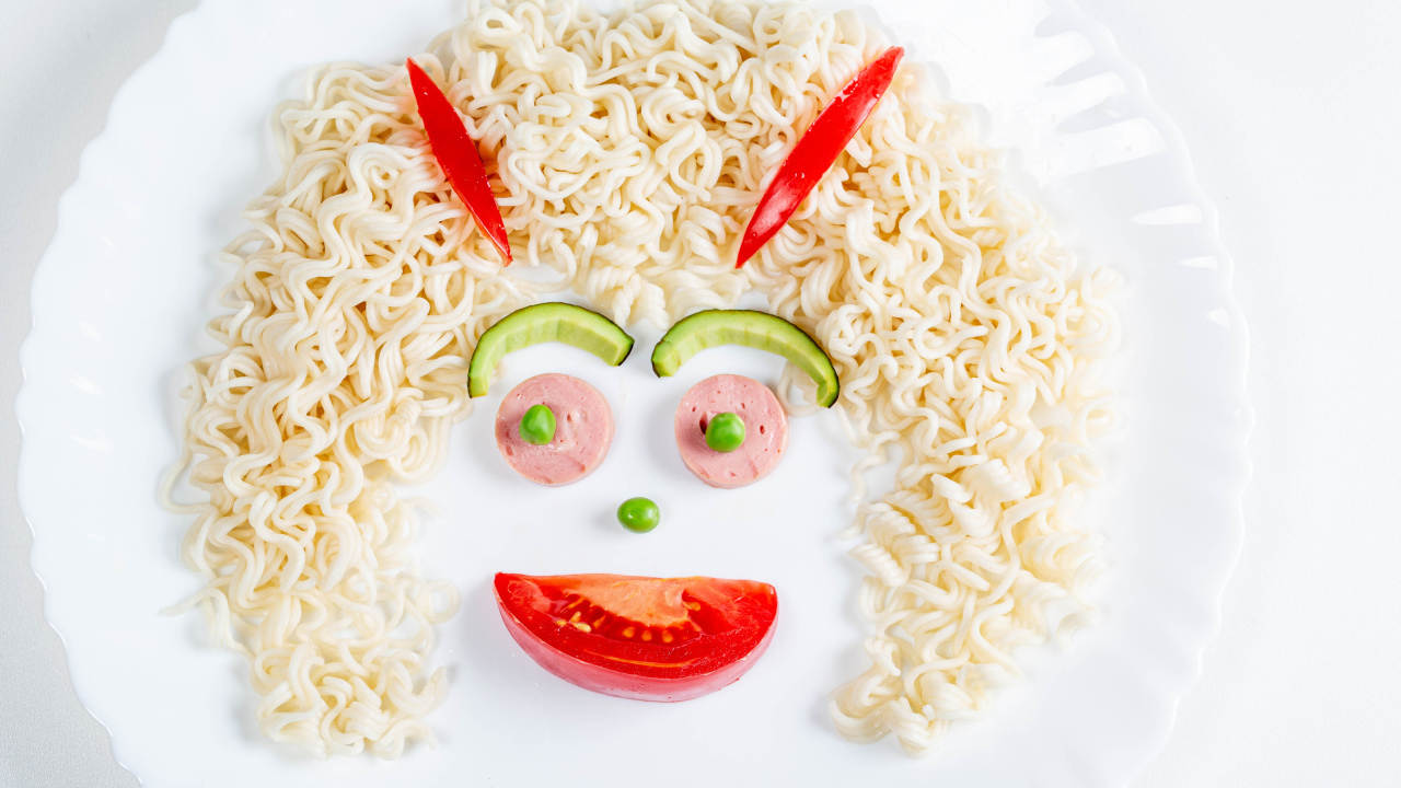 Лицо из вермишели с овощами и колбасой на белой тарелке 