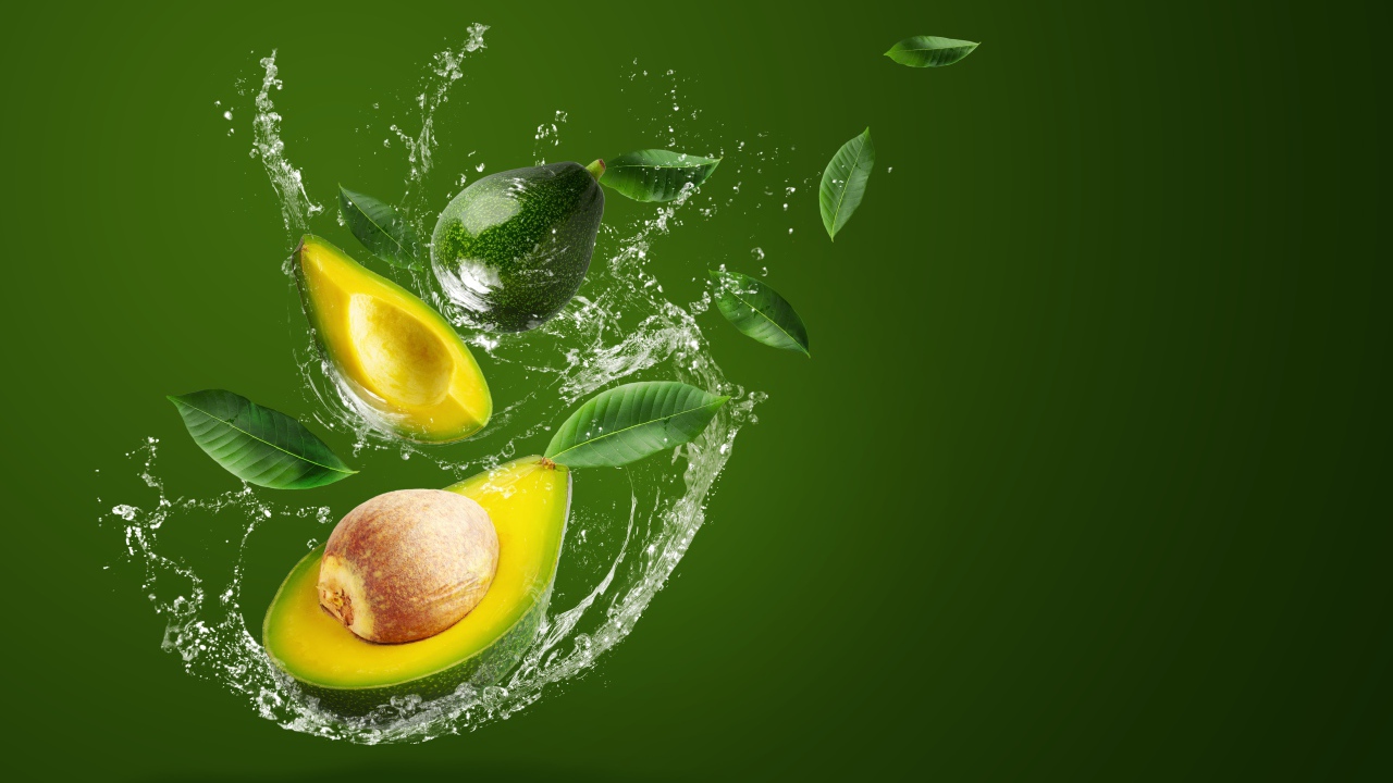 Авокадо в брызгах воды на зеленом фоне