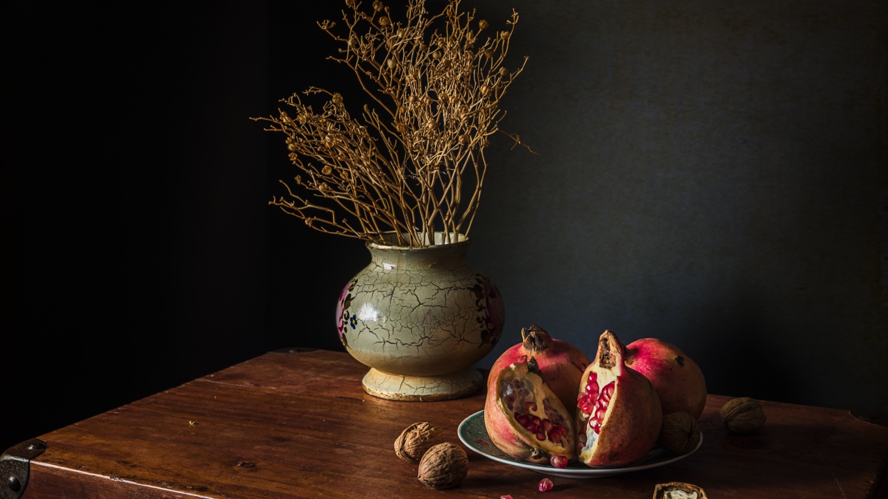 Красный гранат на столе с грецкими орехами и сухой веткой в вазе