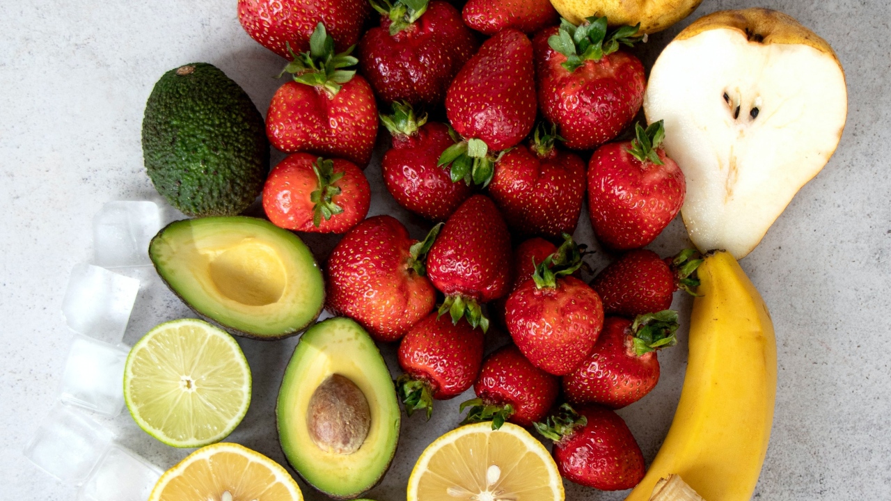 Красная клубника на столе с авокадо, лаймом, грушей и бананом