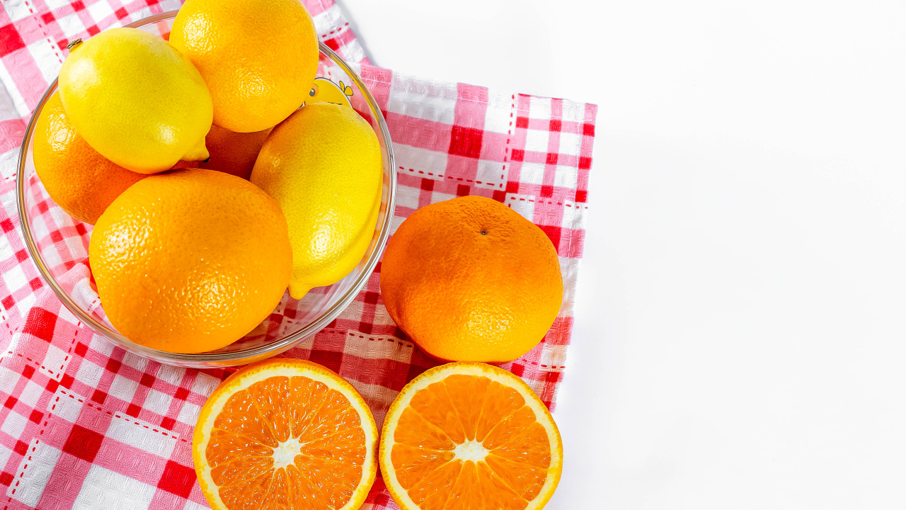 Спелые апельсины и лимоны в стеклянной миске на столе