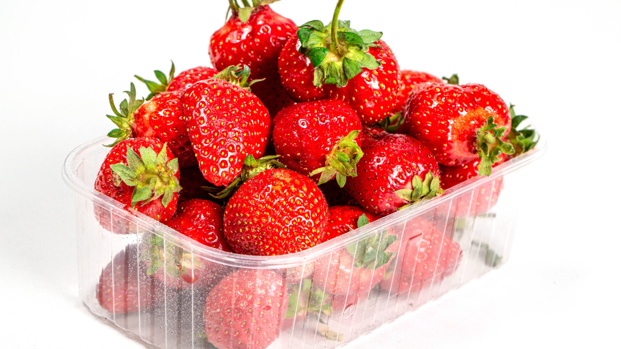 Спелая вкусная клубника в пластиковом контейнере на белом фоне