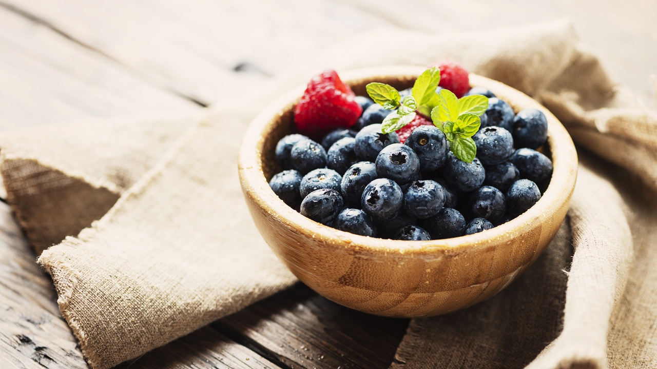 Мокрые ягоды черники в деревянной миске с малиной 