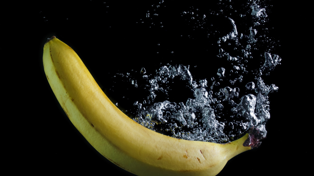 Желтый банан в воде на черном фоне