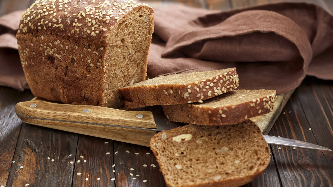 Буханка хлеба нарезанная кусочками на столе с ножом