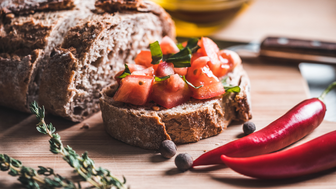 Черный хлеб с кусочками помидора на столе с острым красным перцем