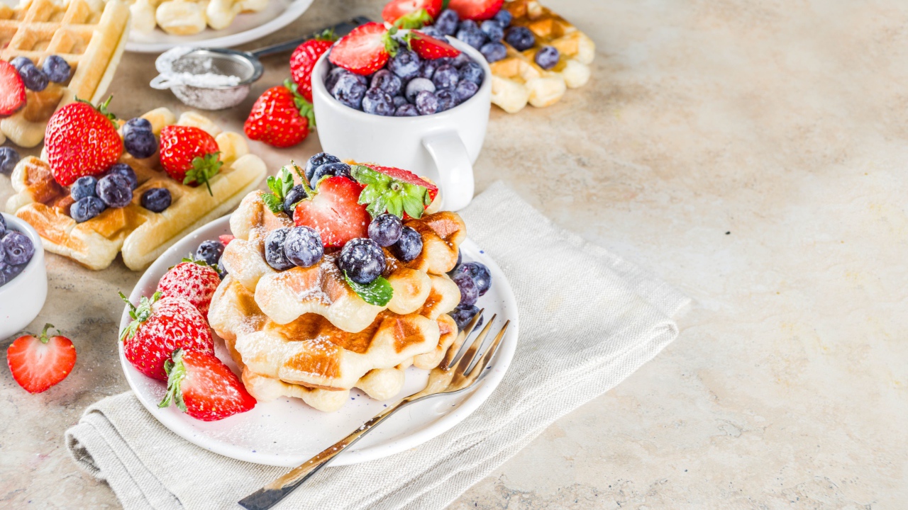 Вкусные сладкие вафли на тарелке с ягодами и сахарной пудрой 