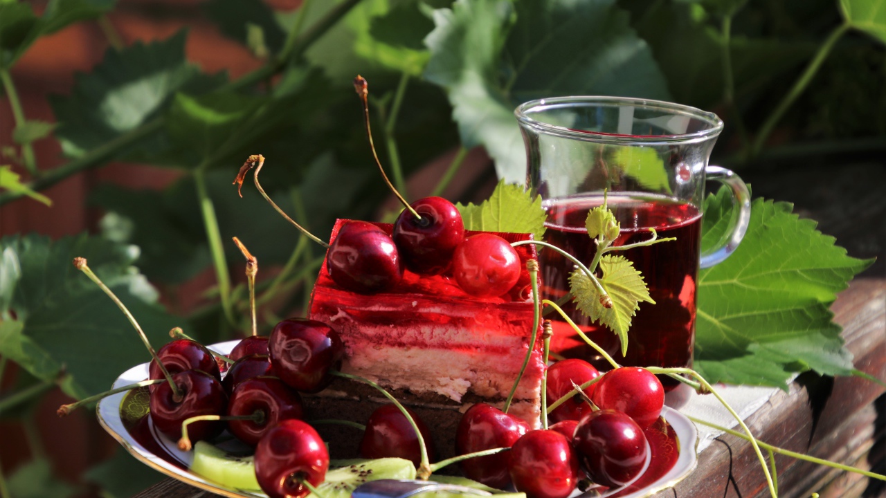 Кусок торта с черешней на столе с чашкой чая 