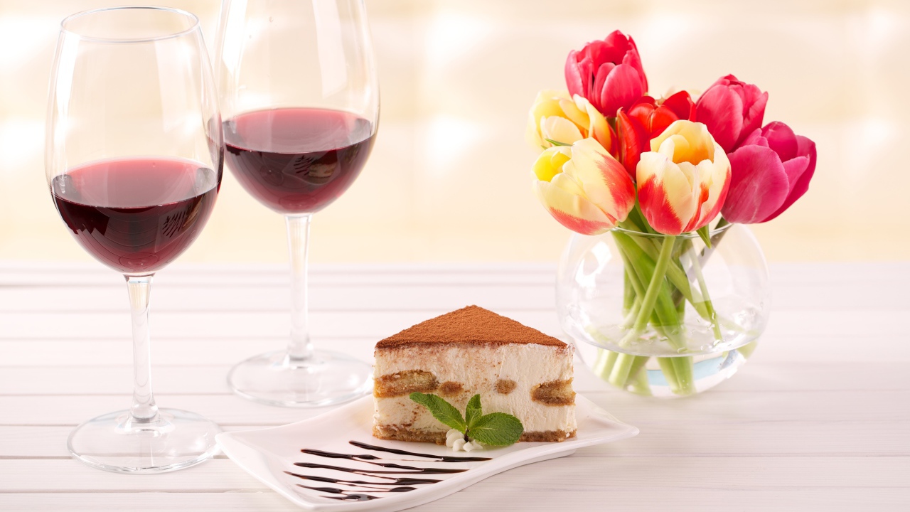 Кусок  тирамису на столе с бокалами вина и букетом тюльпанов
