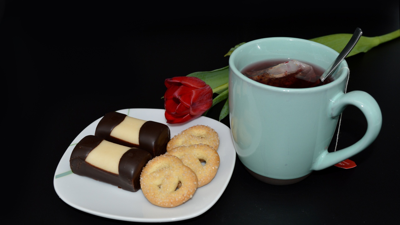 Печенье с конфетами на столе с чашкой чая и тюльпаном