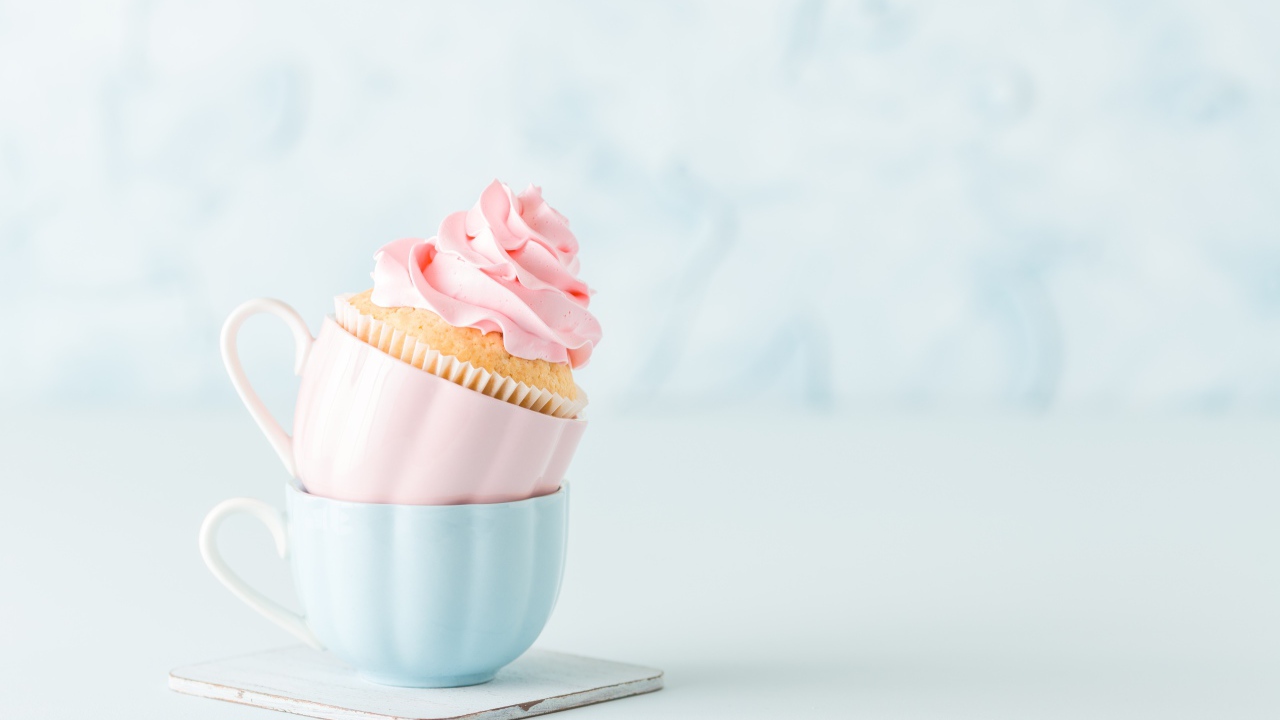 Кекс с розовым кремом с чашками на столе 