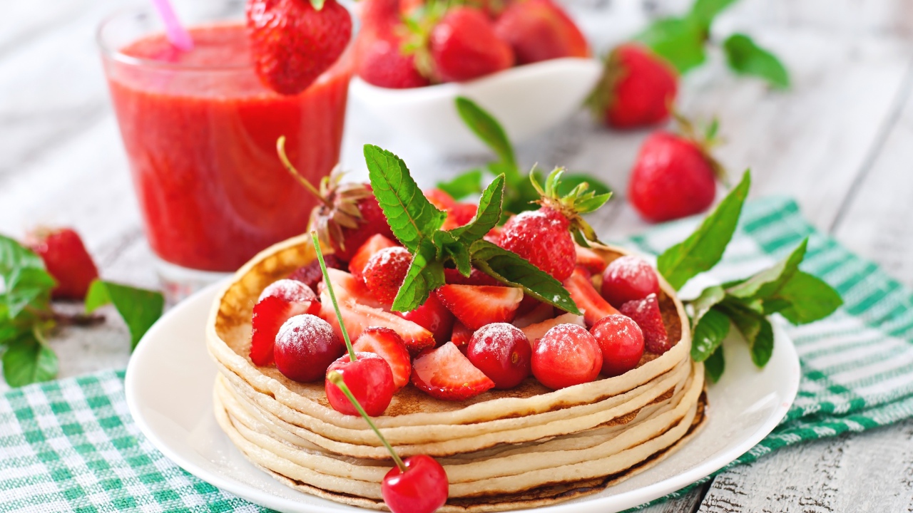 Блины с ягодами клубники  и черешни на белой тарелке