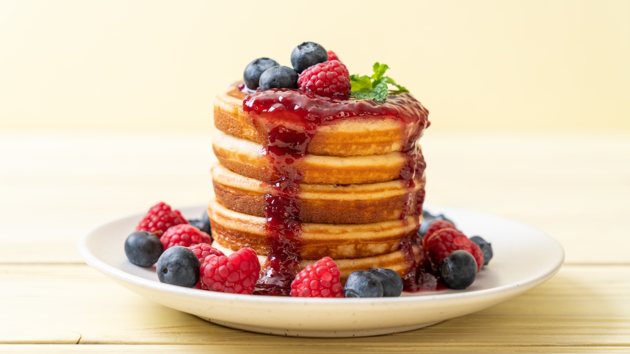 Румяные панкейки с джемом и ягодами черники и малины на тарелке