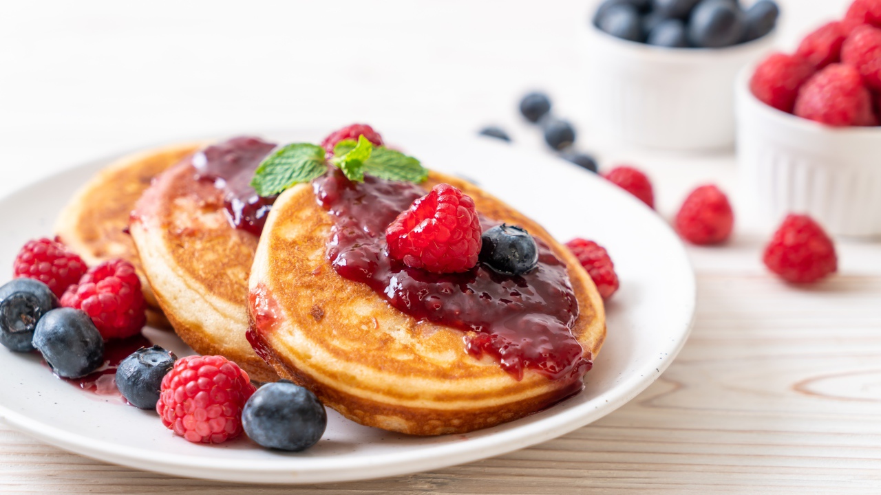 Румяные оладьи с джемом на тарелке с ягодами черники и малины